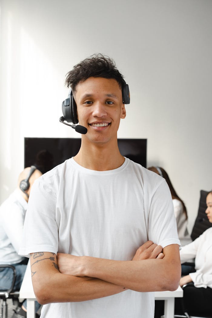 Smiling call center agent in a white shirt wearing a headset in an office setting.
